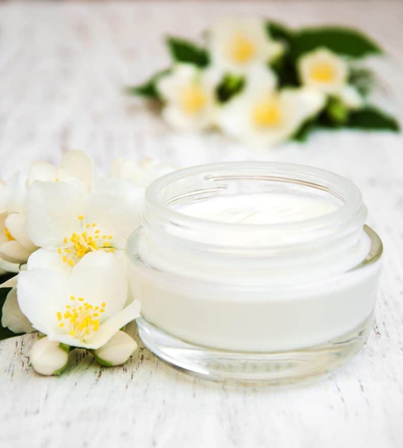 face and body cream moisturizers with jasmine flowers on white wooden background